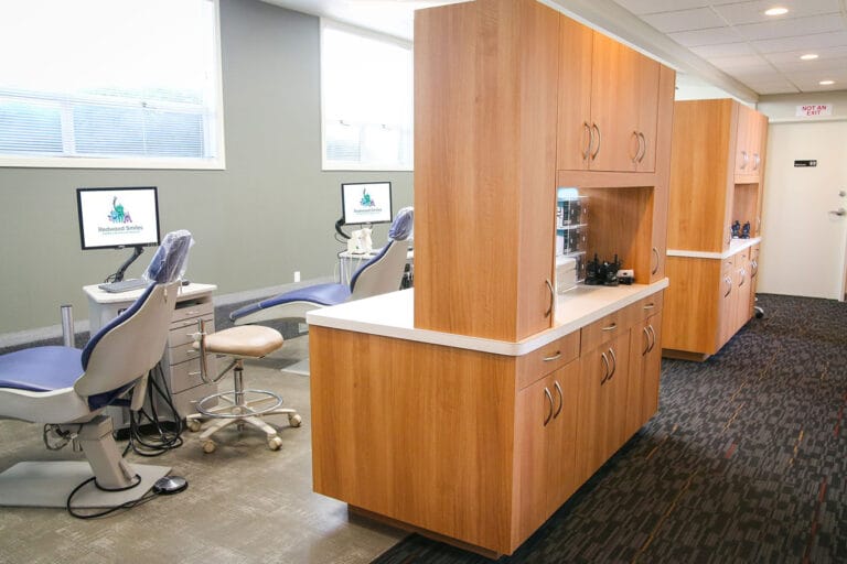 A modern dental clinic with dental chairs, computer monitors, and wooden cabinetry dividing each treatment area.