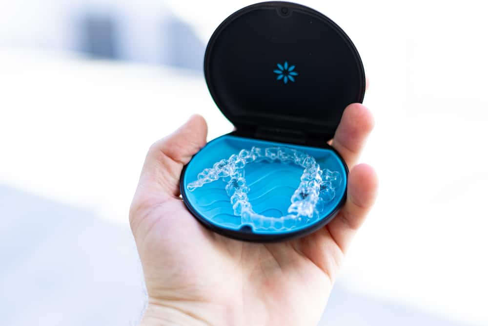 A hand holding an open black and blue case containing a clear dental aligner.